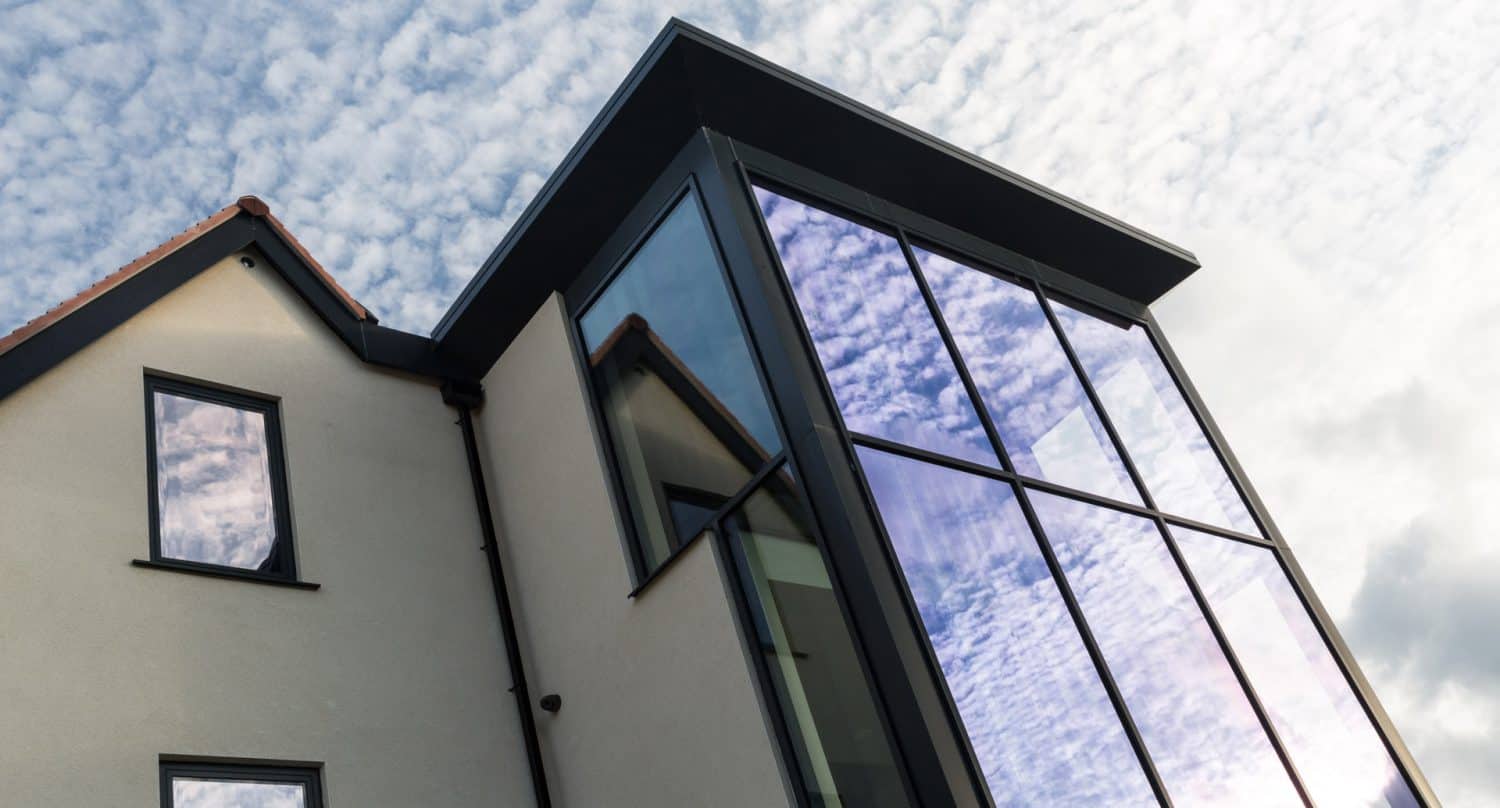 Modern building with cream walls and large, reflective glass windows, showing the cloudy sky. The design features sharp angles and a mix of traditional and contemporary architectural elements.