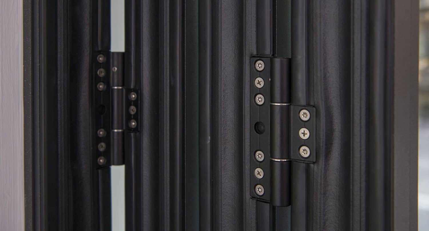 Close-up view of black metal door hinges attached to modern bifold doors. The hinges, fastened with several screws, connect two vertical door panels for a sleek look.