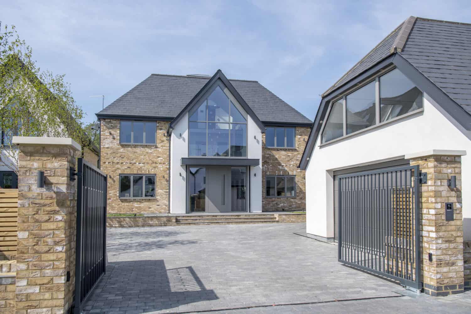 Open driveway gates with a view to a luxury home and detached garage on the side