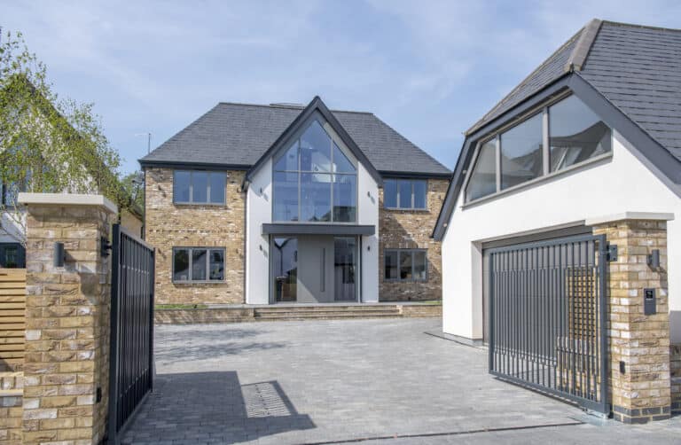 Open driveway gates with a view to a luxury home and detached garage on the side