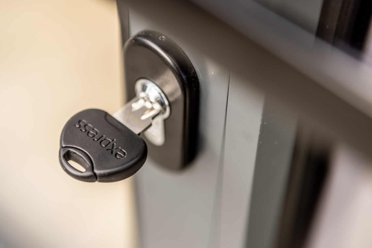 A close-up of a black key labeled express inserted into a lock on a gray metal door, commonly found on modern sliding doors.
