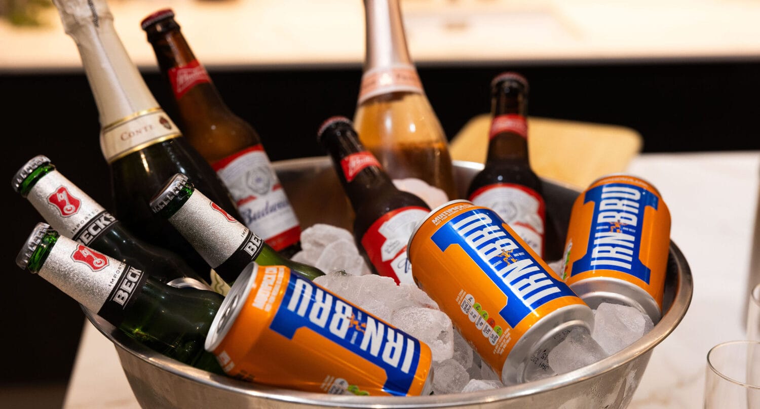 A metal bowl filled with ice holds bottles of beer, cider, and several cans of Irn-Bru soft drink on a countertop, perfectly complementing gatherings near elegant sliding doors or bespoke glass solutions.