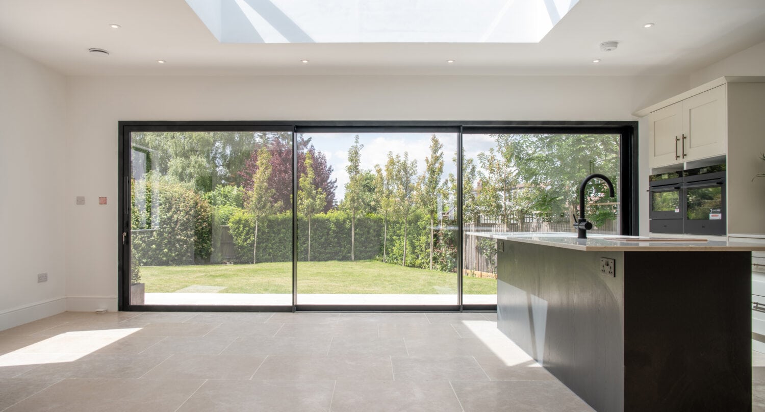 Large black bi-folding glass doors opening to a lush garden, providing natural light and seamless indoor-outdoor living in a contemporary kitchen.