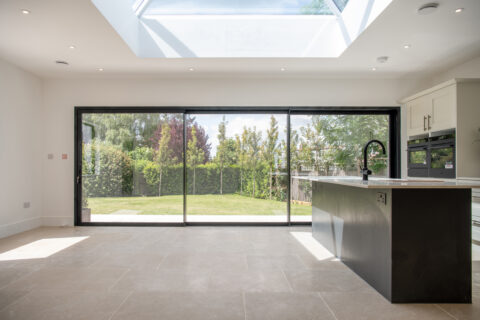 Large black bi-folding glass doors opening to a lush garden, providing natural light and seamless indoor-outdoor living in a contemporary kitchen.