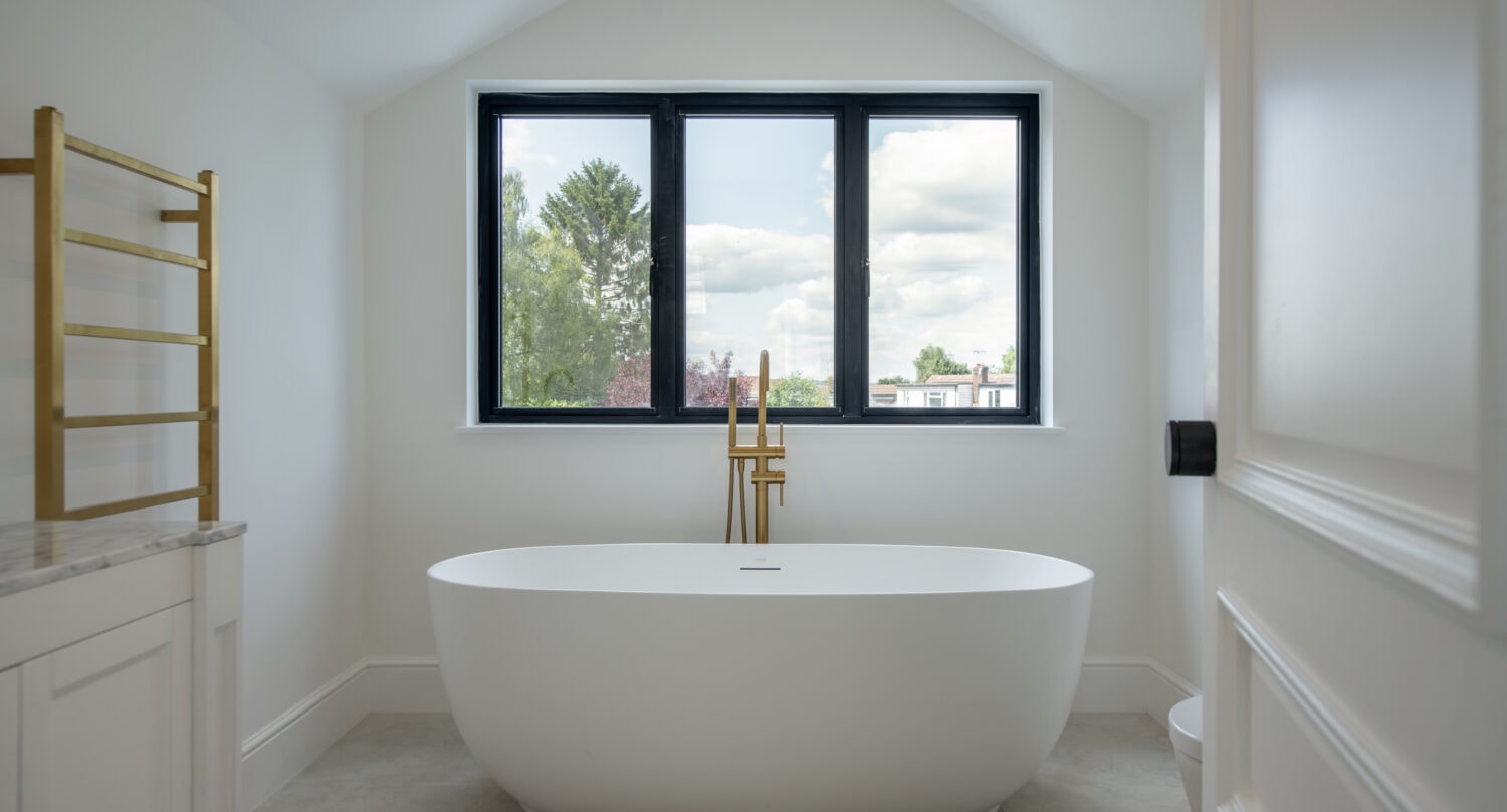 Bright bathroom featuring a large black-framed window, white walls, and a sleek freestanding bathtub, creating a spacious and contemporary feel.
