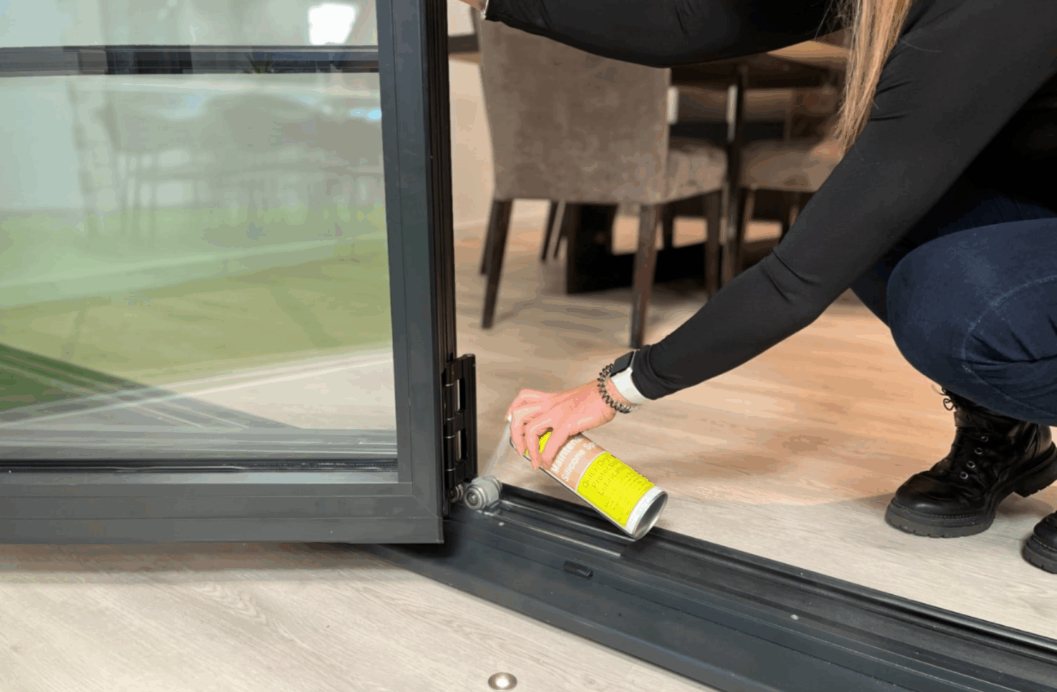 Person applying lubricant to a bifold door track to ensure smooth operation during winter. Focus on maintenance for bi-fold and sliding doors to withstand cold weather.