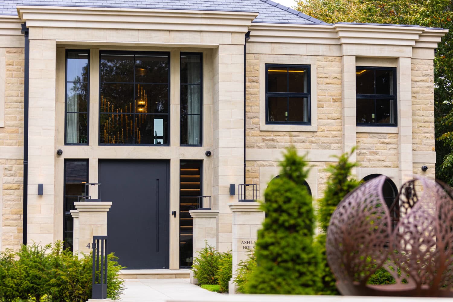 Elegant black pivot door installed in a contemporary stone house exterior, showcasing sleek design and high-quality craftsmanship. Perfect for enhancing curb appeal and security.