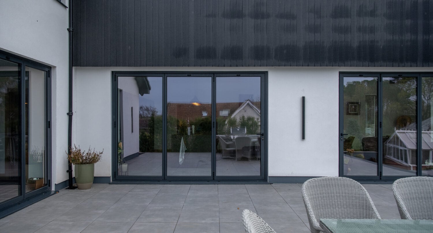 Modern black aluminium bi-folding doors opening to a stylish outdoor patio, enhancing natural light and outdoor views for The Garden House, Aberdeen.