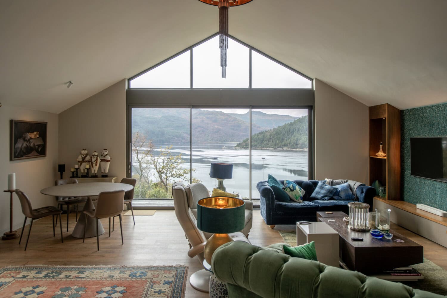 Stunning interior view featuring large bi-folding doors opening to scenic lake and mountain views at Norse Lodge, Helensburgh. Perfect for seamless indoor-outdoor living.