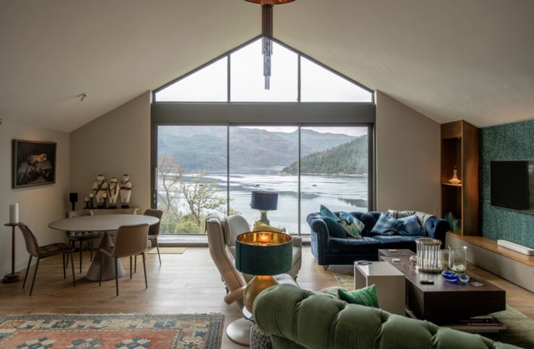 Stunning interior view featuring large bi-folding doors opening to scenic lake and mountain views at Norse Lodge, Helensburgh. Perfect for seamless indoor-outdoor living.