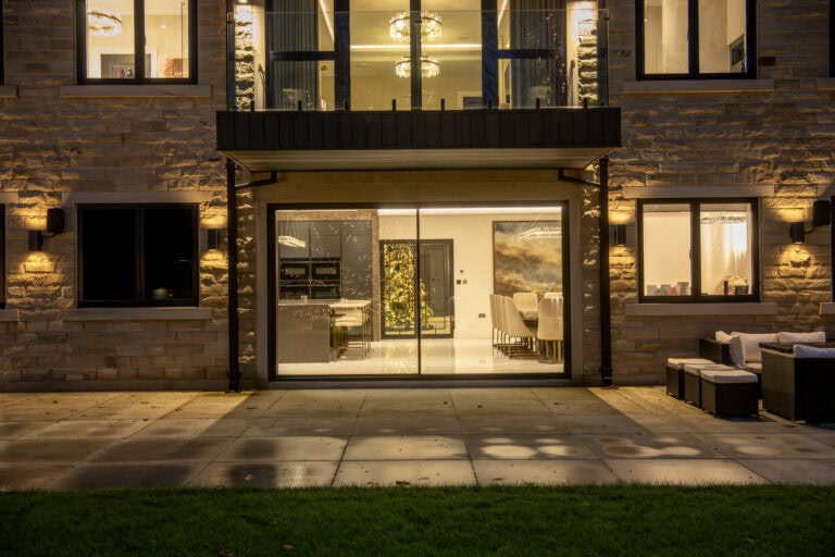 Modern sliding bi-fold door system at night, showcasing seamless indoor-outdoor transition with large glass panels and sleek black frames.