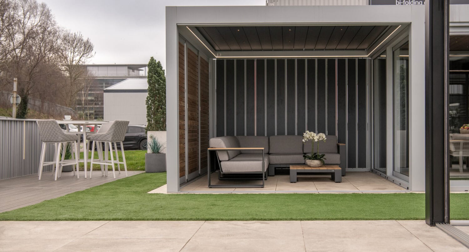 Contemporary garden room with glazed folding sides and outdoor dining space on artificial lawn
