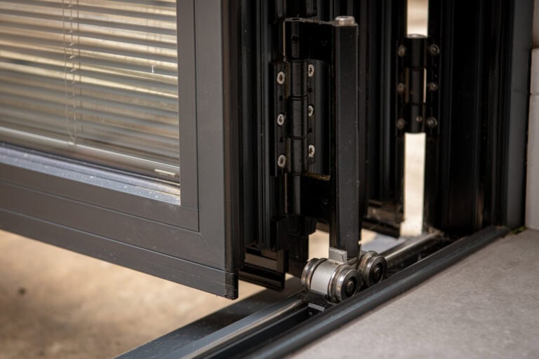Close-up of sliding bi-fold door track and roller system, showcasing durable hardware for smooth opening and closing. Ideal for modern home and commercial spaces.
