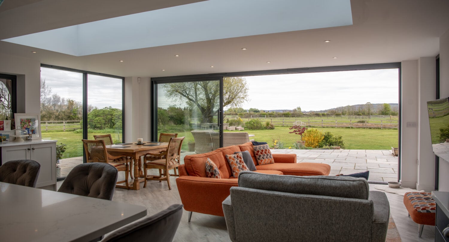 Modern living room with large sliding bi-fold doors opening to a garden, showcasing natural light and outdoor views. Perfect for stylish, functional home design.