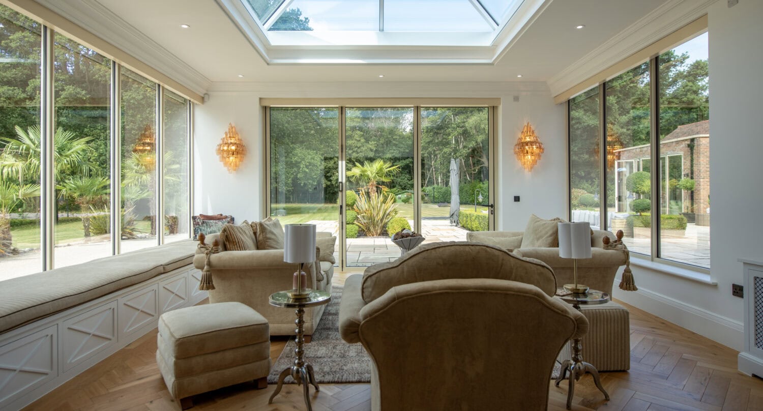 Spacious living room featuring large windows and a skylight, offering natural light and views of a lush garden, with comfortable seating and elegant decor.