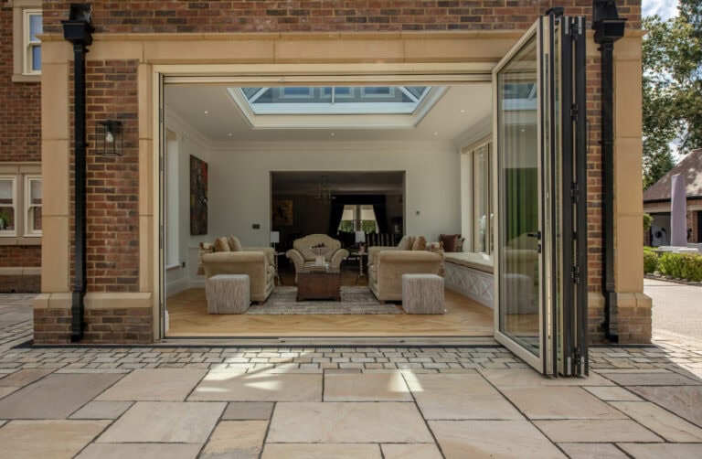 Modern bi-folding doors opening to a spacious, stylish living room with a skylight, creating seamless indoor-outdoor living space at Foxwood House.