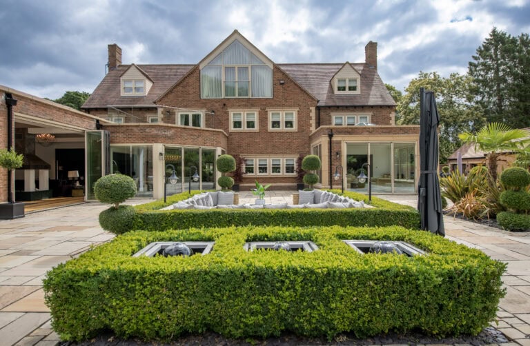 Elegant house with large bi-folding doors opening to a landscaped garden and patio area, showcasing modern outdoor living space.