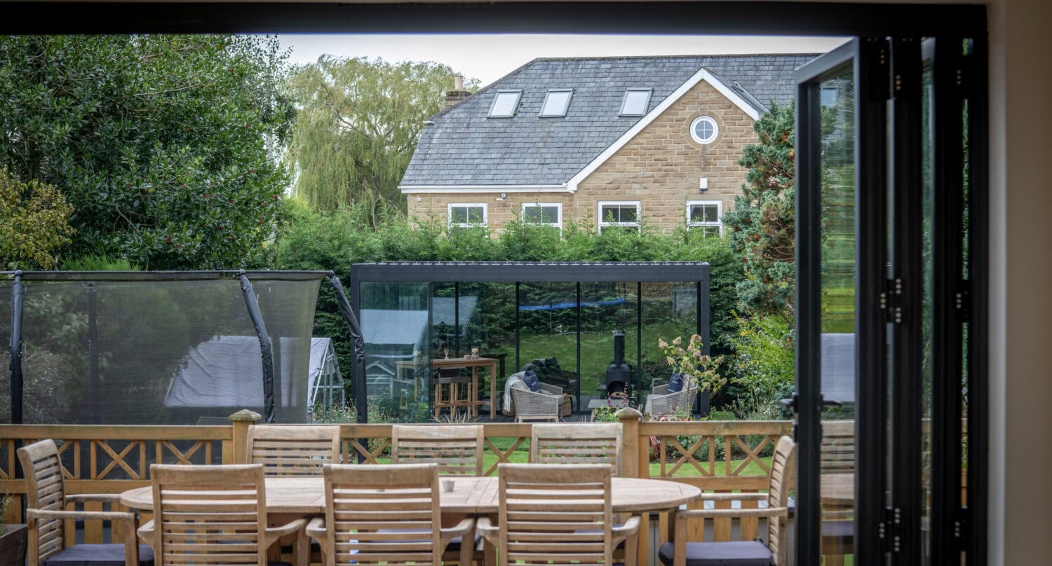 Modern bi-folding doors opening to a spacious outdoor patio with garden furniture and lush greenery, ideal for outdoor living and solar shading solutions.