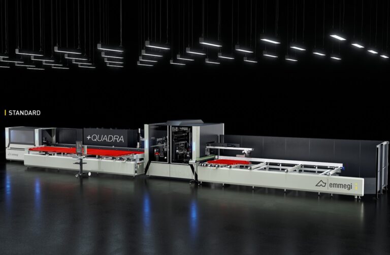 A large, modern industrial machine with the label “QUADRA” and “emmegi,” set in a well-lit factory space with a black background and illuminated ceiling lights—designed for bespoke glass solutions such as sliding doors.