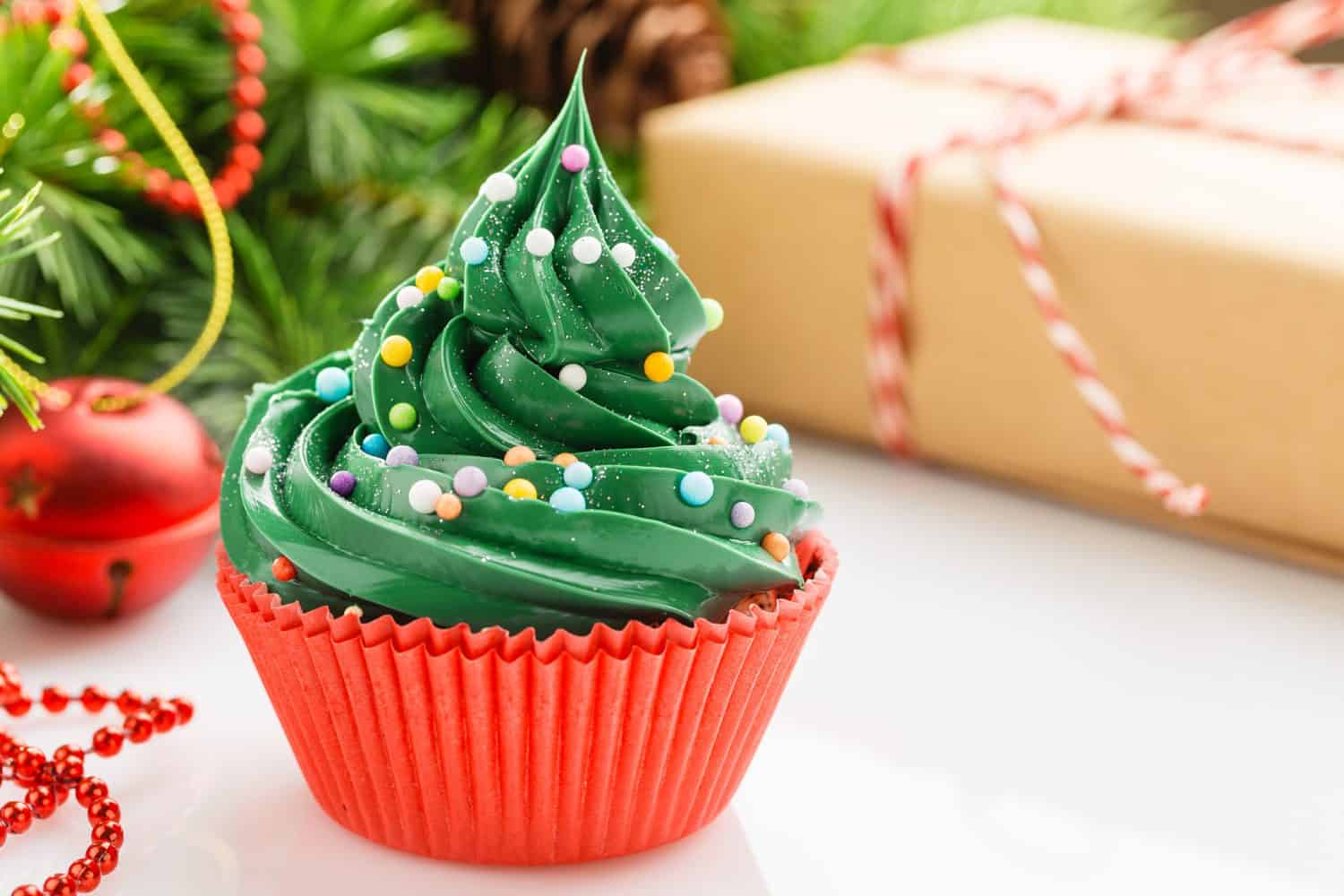 Christmas green cupcake with colorful sprinkles in red cup on white background with decorations