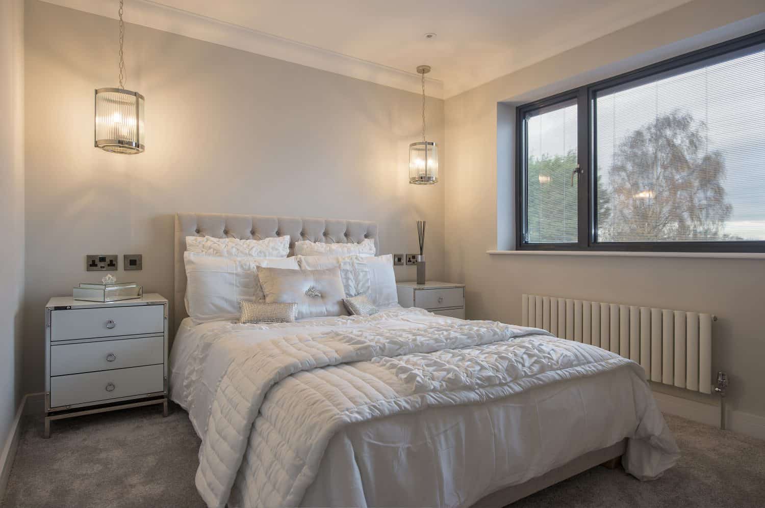 Modern bedroom with a double bed dressed in white bedding, two bedside tables with lamps, and a large window letting in natural light. Elegant sliding doors enhance the neutral decor and add to the room’s cozy, inviting atmosphere.
