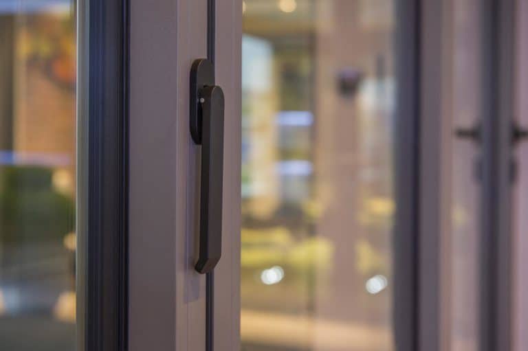 Close-up of a modern black door handle on a glass door, with a softly blurred indoor background featuring warm lighting and muted colors—perfect inspiration for bespoke glass solutions or elegant sliding doors.