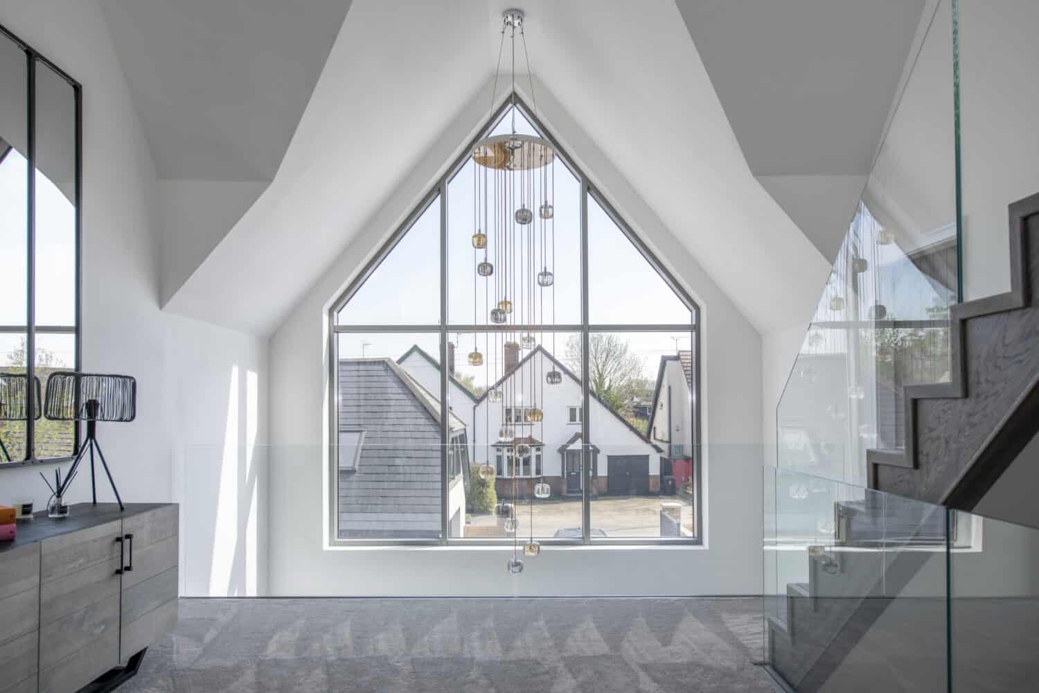 Luxury high ceiling landing featuring large pendant light and shaped aluminum windows
