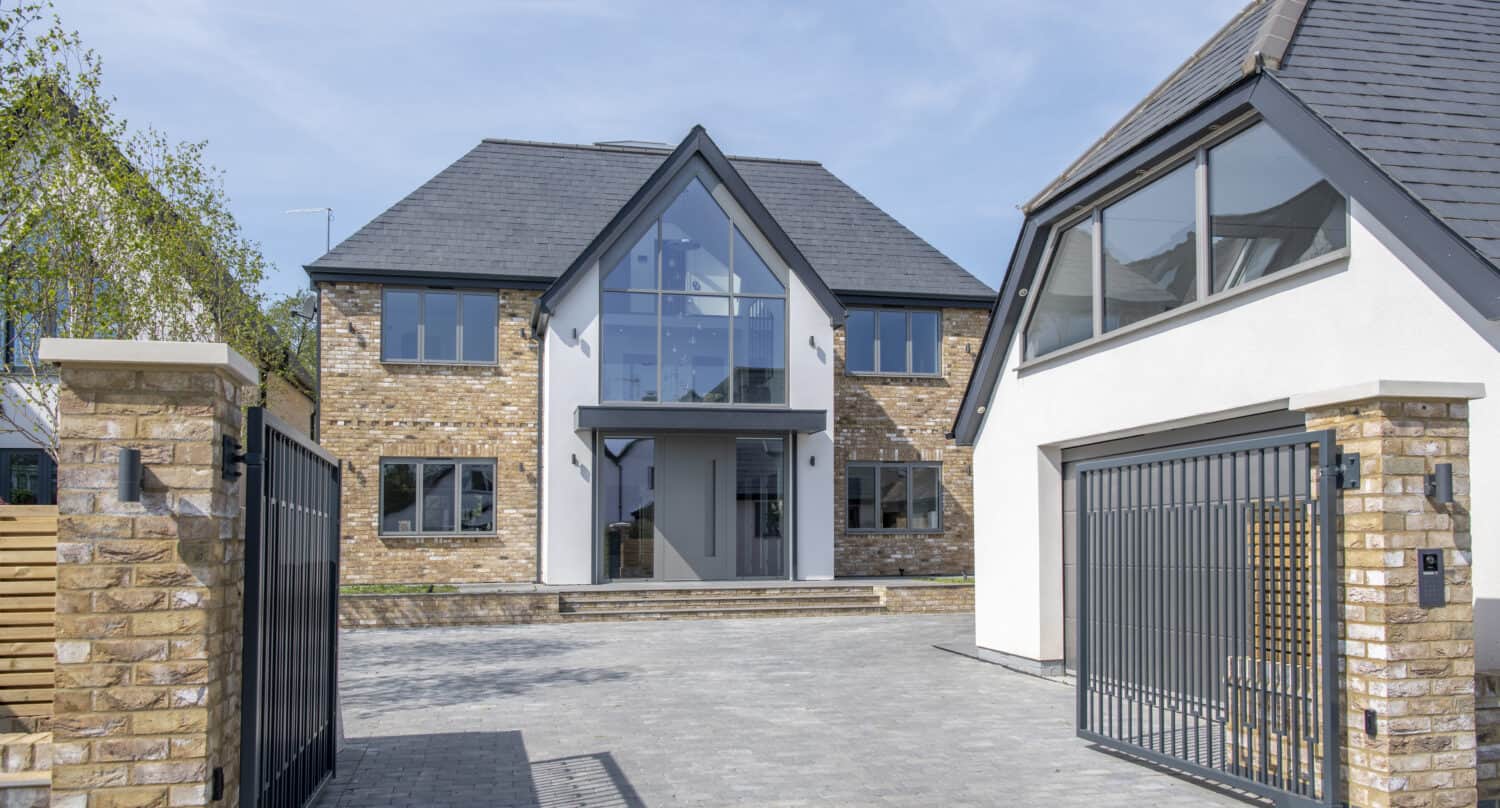 Open driveway gates with a view to a luxury home and detached garage on the side