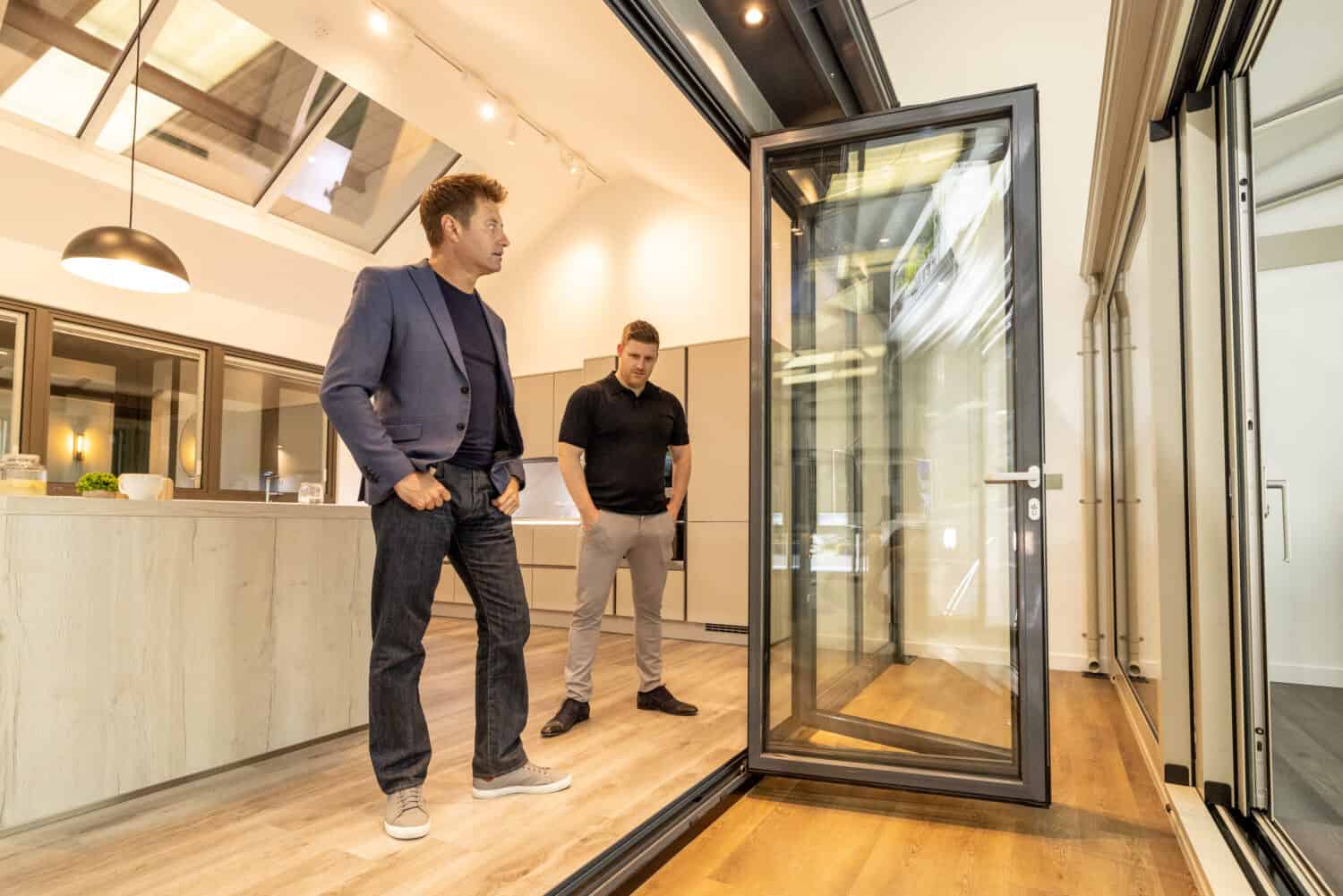 Two men in a modern kitchen looking to a 4 panel bifold doors in a showroom