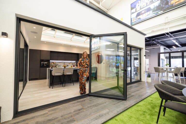 A woman posing in a modern kitchen that's featuring some large bifold doors in a showroom