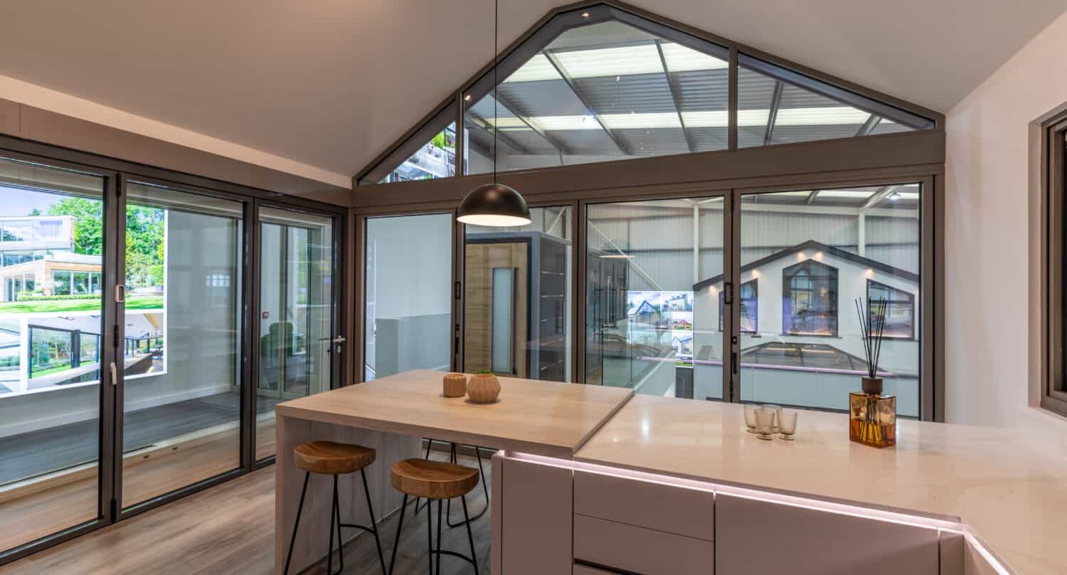 Modern clear kitchen featuring wide aluminium bi folding doors and shaped windows in a showroom