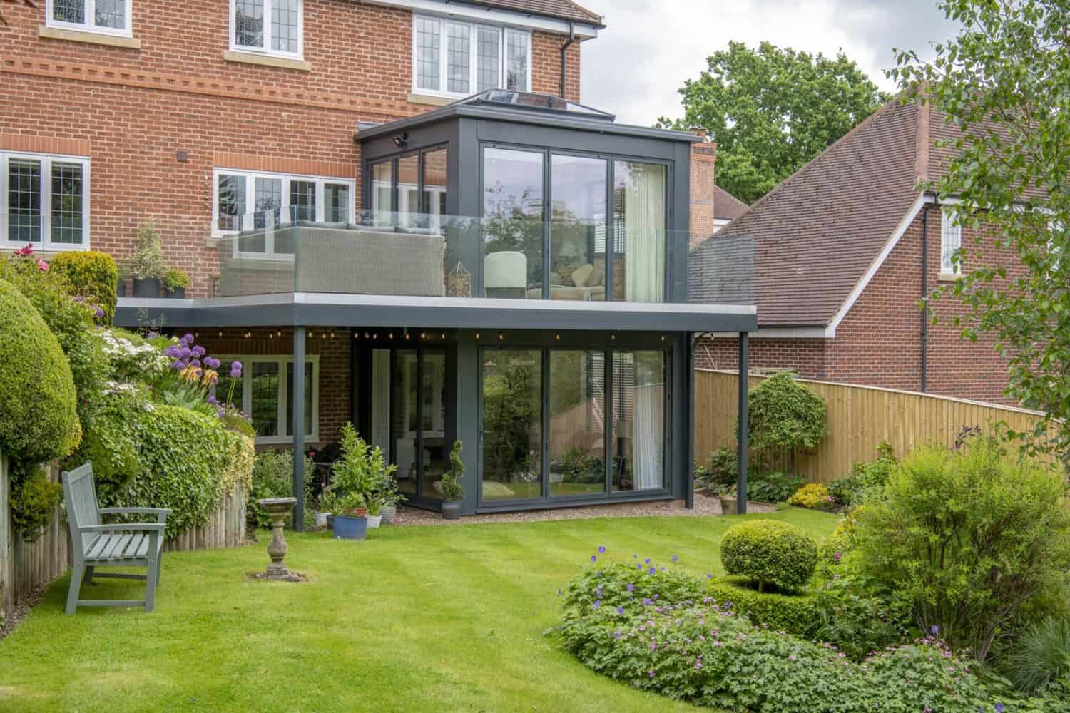 Modern home extension featuring black bifolding doors and a terrace in the first floor with balustrade glass