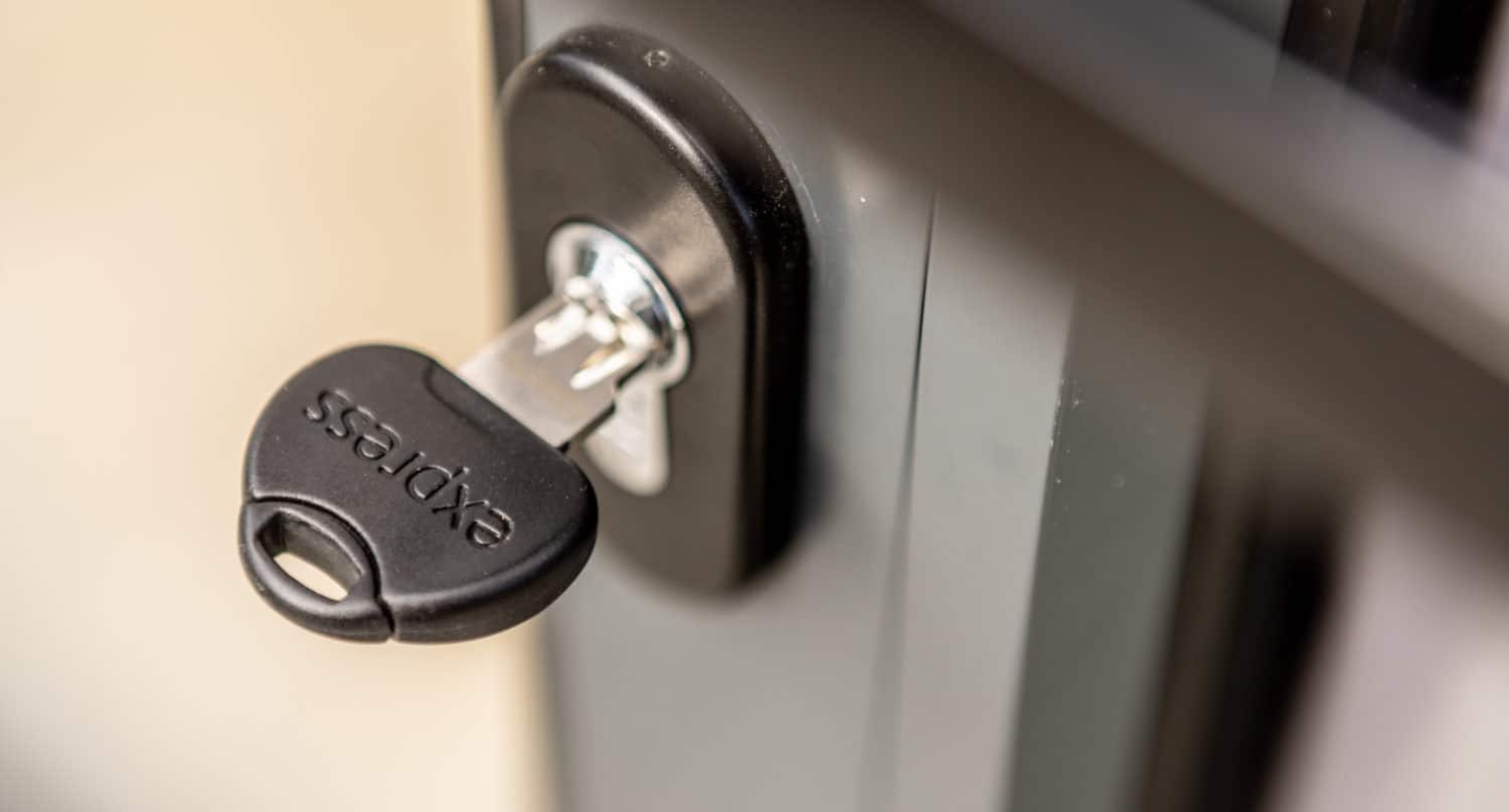 A close-up of a black key labeled express inserted into a lock on a gray metal door, commonly found on modern sliding doors.