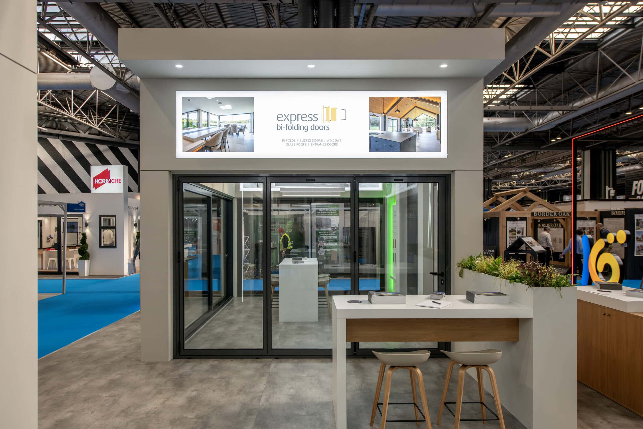 Modern exhibition stand showcasing Express Bi-Folding Doors with sleek glass doors and contemporary design at a trade show.