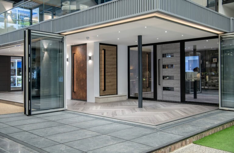 Modern home exterior with large bifold doors and glass roofing opens to a spacious indoor area featuring wood and tile floors, sleek paneling, and minimalist lighting, blending indoor and outdoor spaces seamlessly.