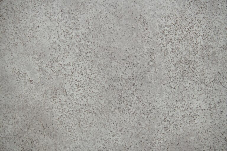A close-up view of a textured gray concrete surface with scattered small dark specks and an uneven, mottled appearance—an ideal backdrop for showcasing modern sliding doors or bespoke glass solutions.