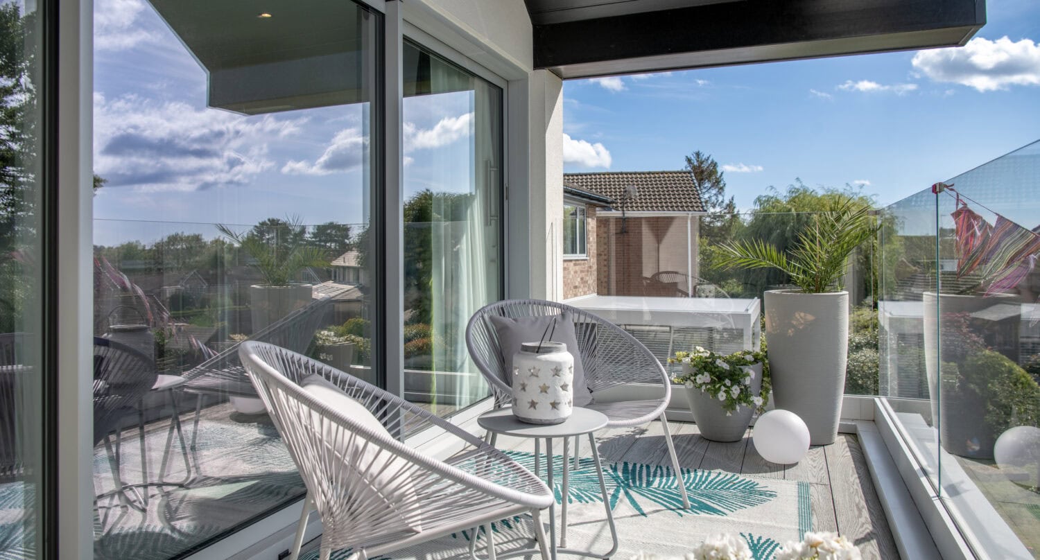 Modern balcony with large glass bi-folding doors, outdoor seating, and scenic views in Harrogate. Perfect for stylish indoor-outdoor living and enhancing home aesthetics.