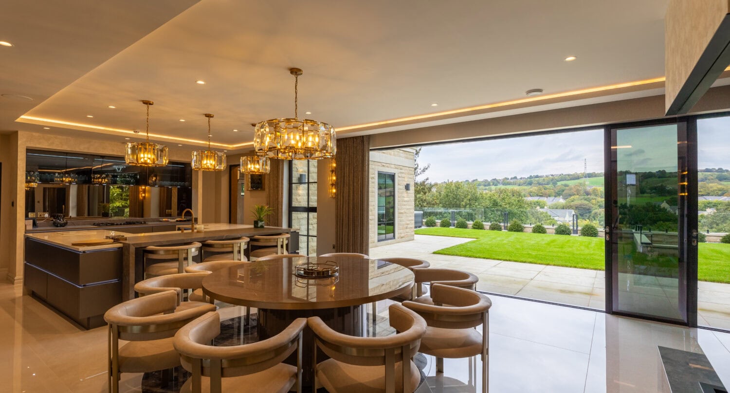 Spacious indoor dining area featuring large glass bi-fold doors that open to a lush outdoor garden, perfect for modern luxury living and seamless indoor-outdoor entertaining.