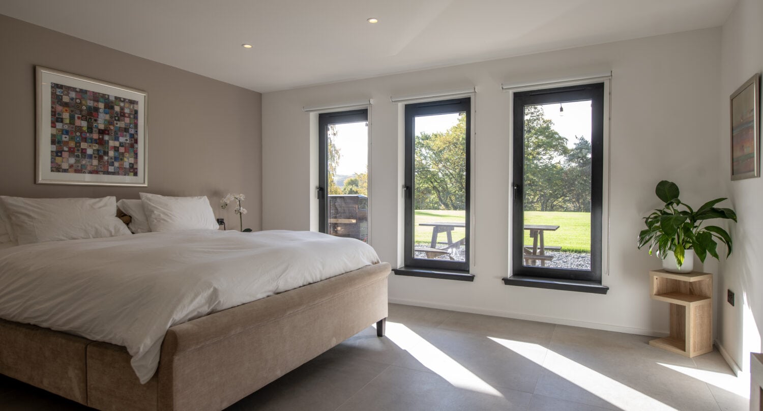 Bright bedroom featuring large bi-folding doors opening to a garden view, perfect for natural light and outdoor access at Orchard Farm, Crossford.
