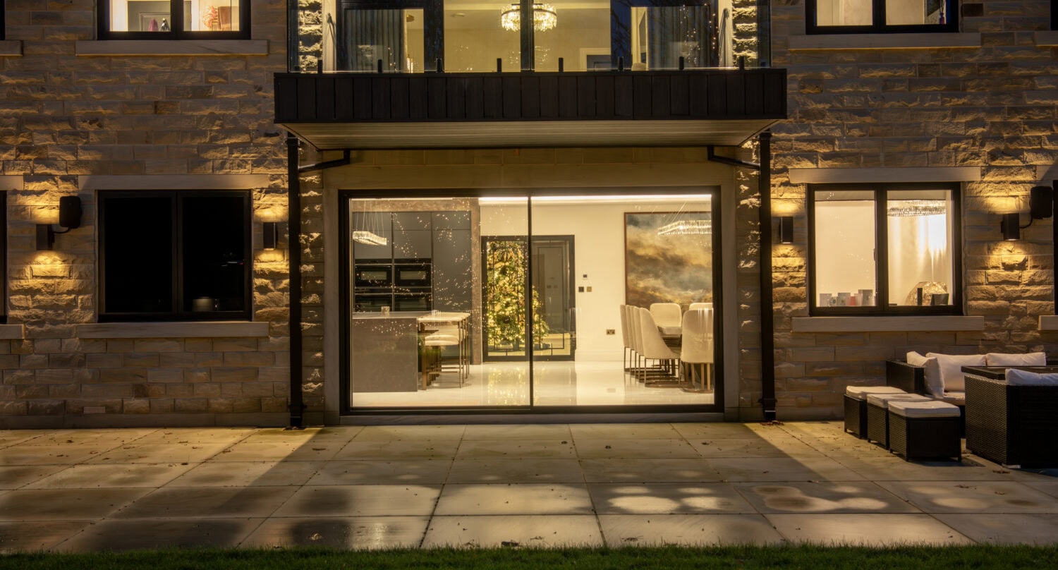 Modern sliding bi-fold door system at night, showcasing seamless indoor-outdoor transition with large glass panels and sleek black frames.