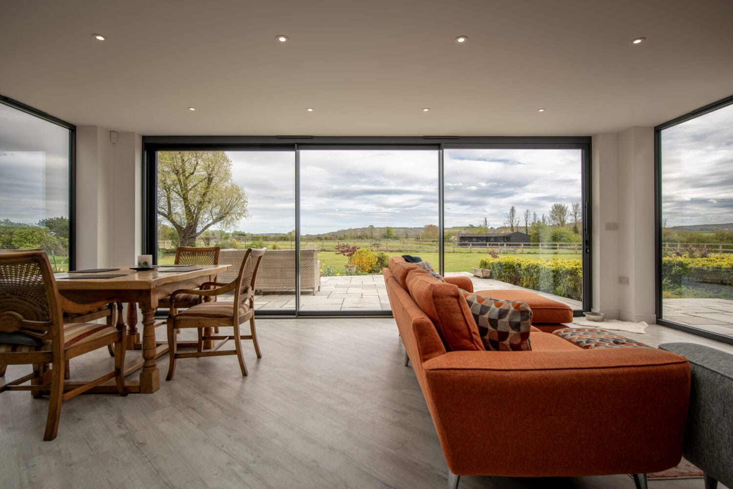 Large glass bi-folding doors opening to a scenic garden, providing natural light and a spacious feel to the living area. Perfect for stylish, energy-efficient home upgrades.