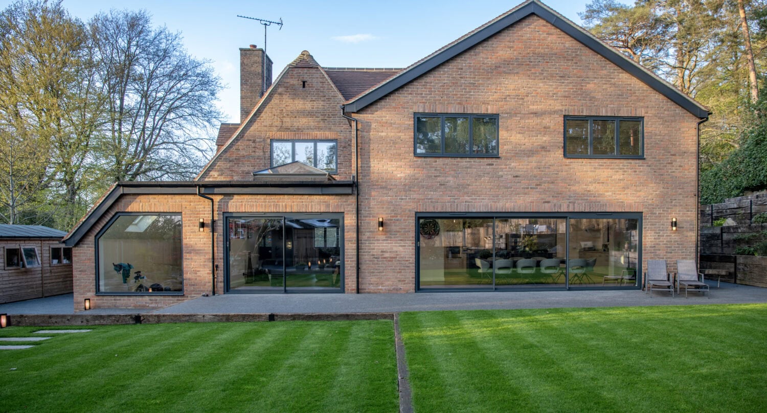 Contemporary brick house featuring large bi-folding doors that open to a lush green garden, providing seamless indoor-outdoor living space.