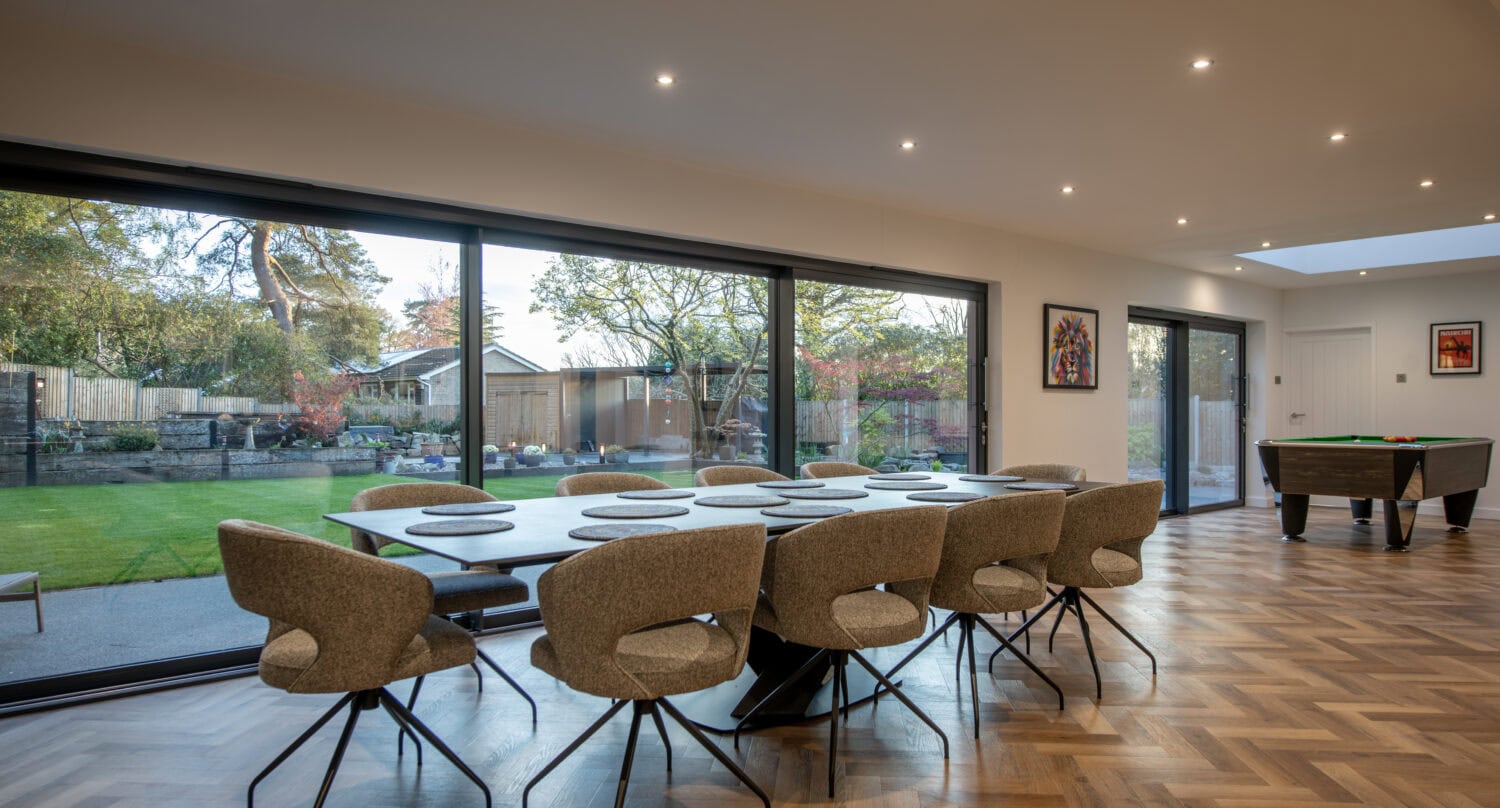 Elegant indoor dining space featuring expansive bi-fold doors that seamlessly connect the interior with outdoor garden views.