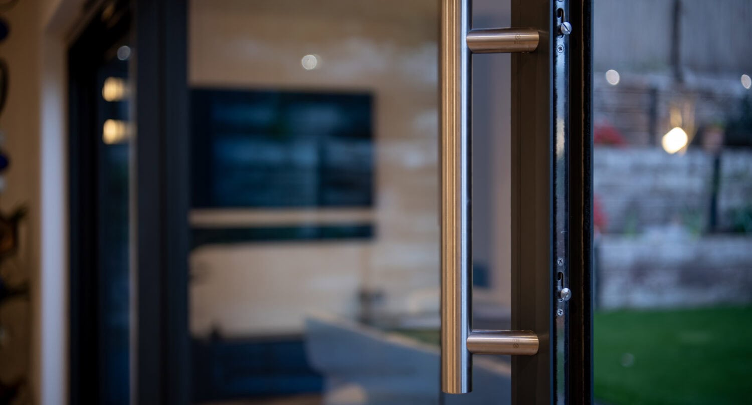 Aluminium bi-fold door featuring sleek handle and large glass panels, ideal for connecting indoor living spaces with outdoor patios, enhancing natural light and aesthetic appeal.