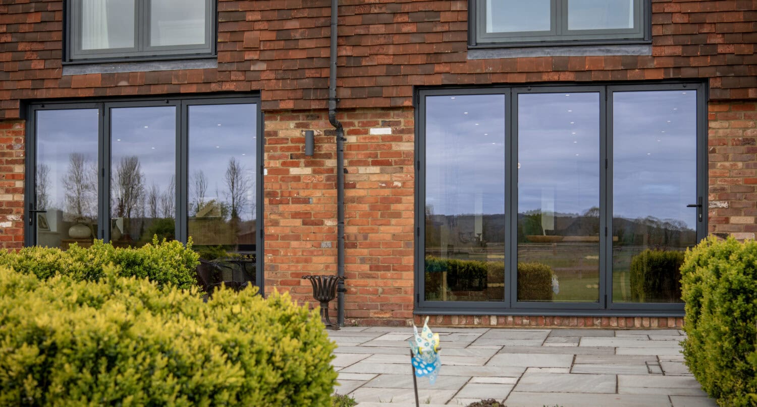 Modern black sliding bi-fold doors installed in a brick house, providing seamless indoor-outdoor living space and enhancing natural light.