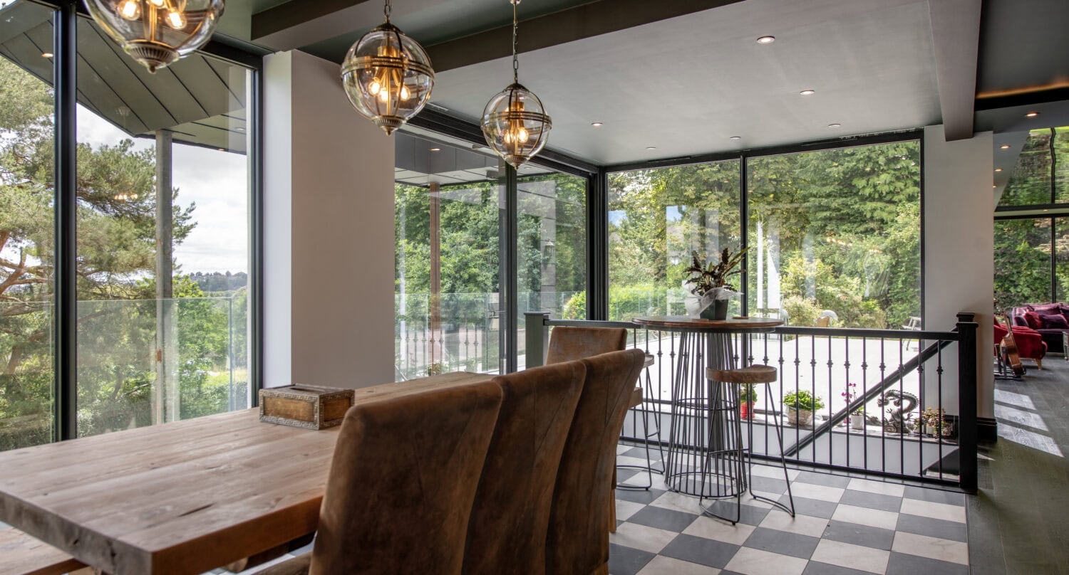 Modern interior featuring large bi-folding doors opening to lush greenery, with a dining area and stylish lighting fixtures at Stumperlowe Hall.