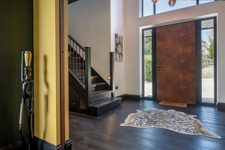 Modern entrance hall with large glass doors, dark wood flooring, and a staircase, featuring contemporary decor and natural light.
