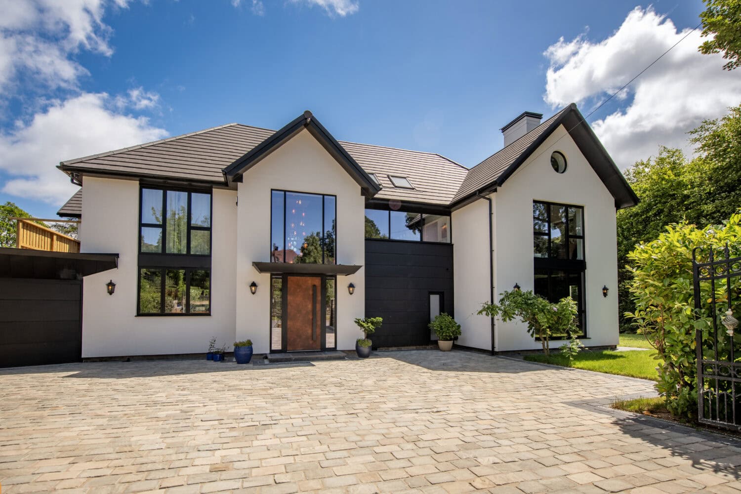 Contemporary house featuring large bi-folding doors, modern design, and a spacious driveway, set against a bright blue sky with some clouds.