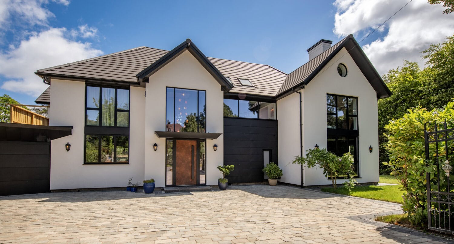 Contemporary house featuring large bi-folding doors, modern design, and a spacious driveway, set against a bright blue sky with some clouds.