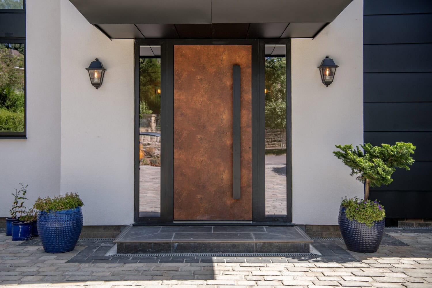Modern entrance with bi-folding doors and rust-coloured front door at Stumperlowe Hall, featuring outdoor lighting and potted plants.